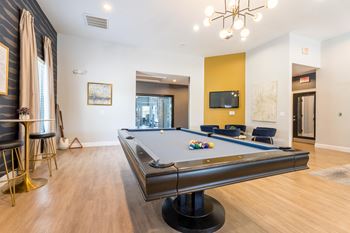 A pool table is in the middle of a room with a chair and a tv.